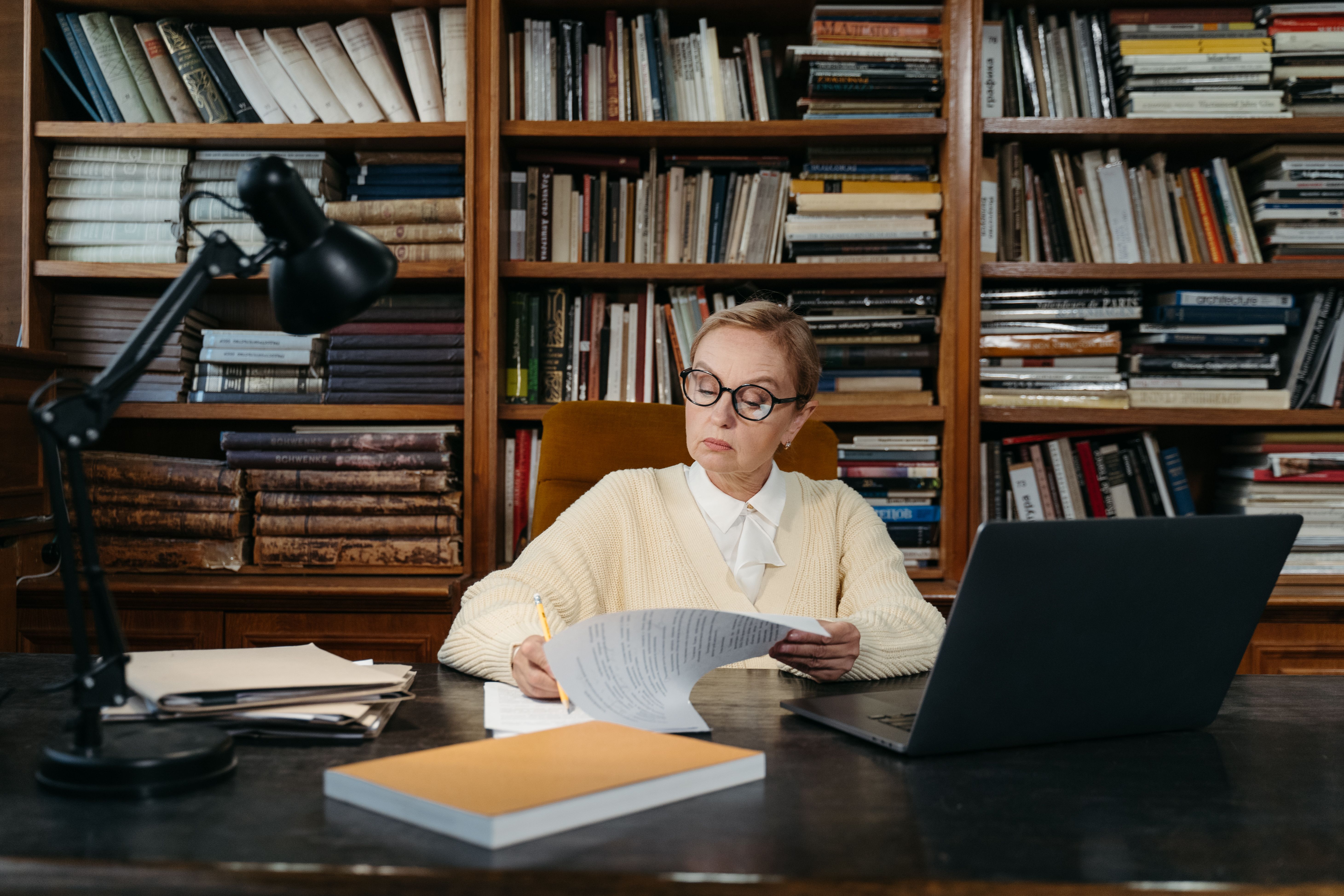 Researcher reviewing documents at a desk surrounded by books and a laptop, illustrating scholarly publication review.