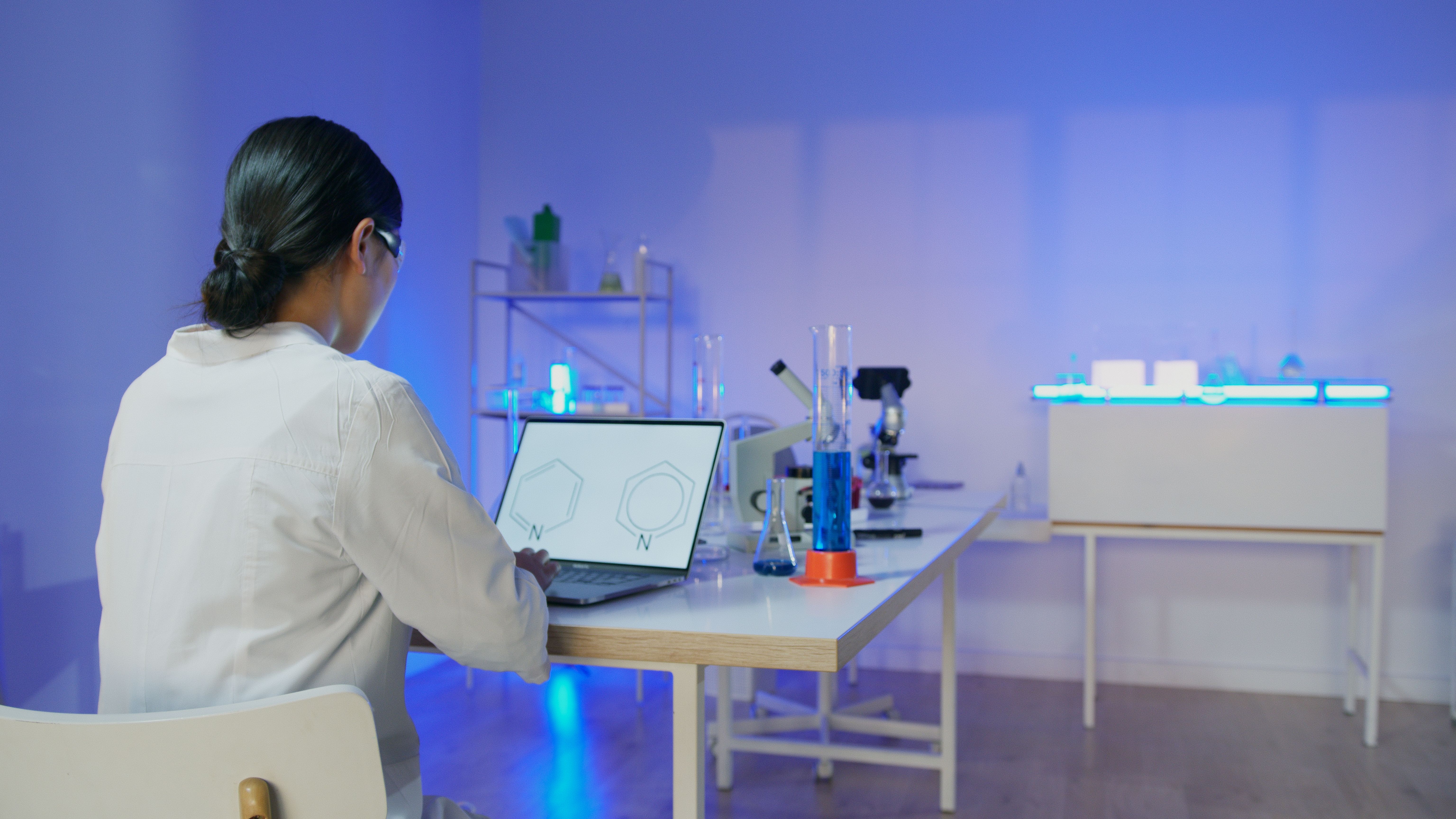 Female scientist studying chemical structures on a laptop in a modern laboratory.